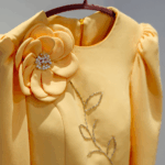 Golden yellow peplum jacket with hand-beaded floral appliqué and matching tulle skirt on hanger.