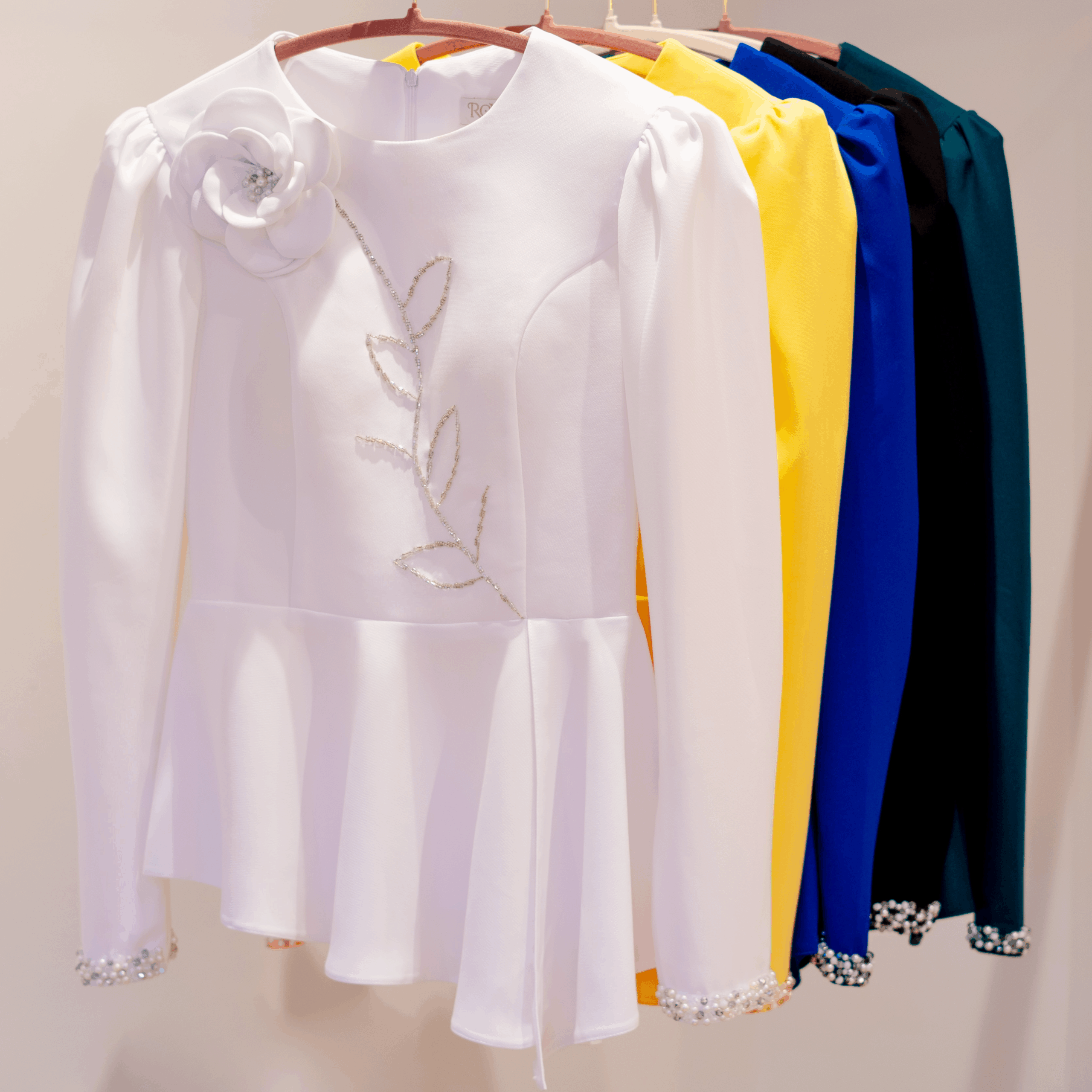 Royaé FLORENCIA couture jackets displayed in white, golden yellow, royal blue, black, and dark green on a clothing rail.