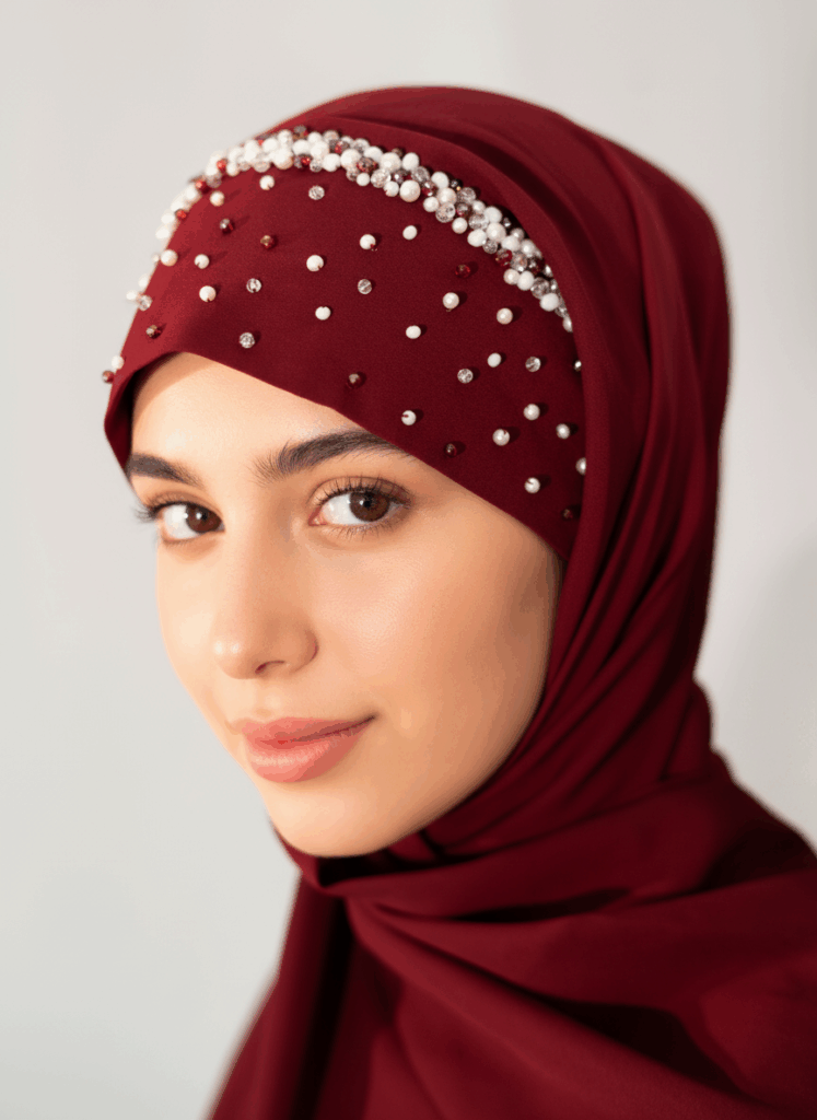 A model wearing a burgundy Pearl Tuck-In Hijab with pearl and crystal embellishments.