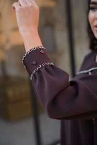 Close-up of handmade deep mauve brown waterfall dress sleeve with hand-embroidered stone and bead embellishments.