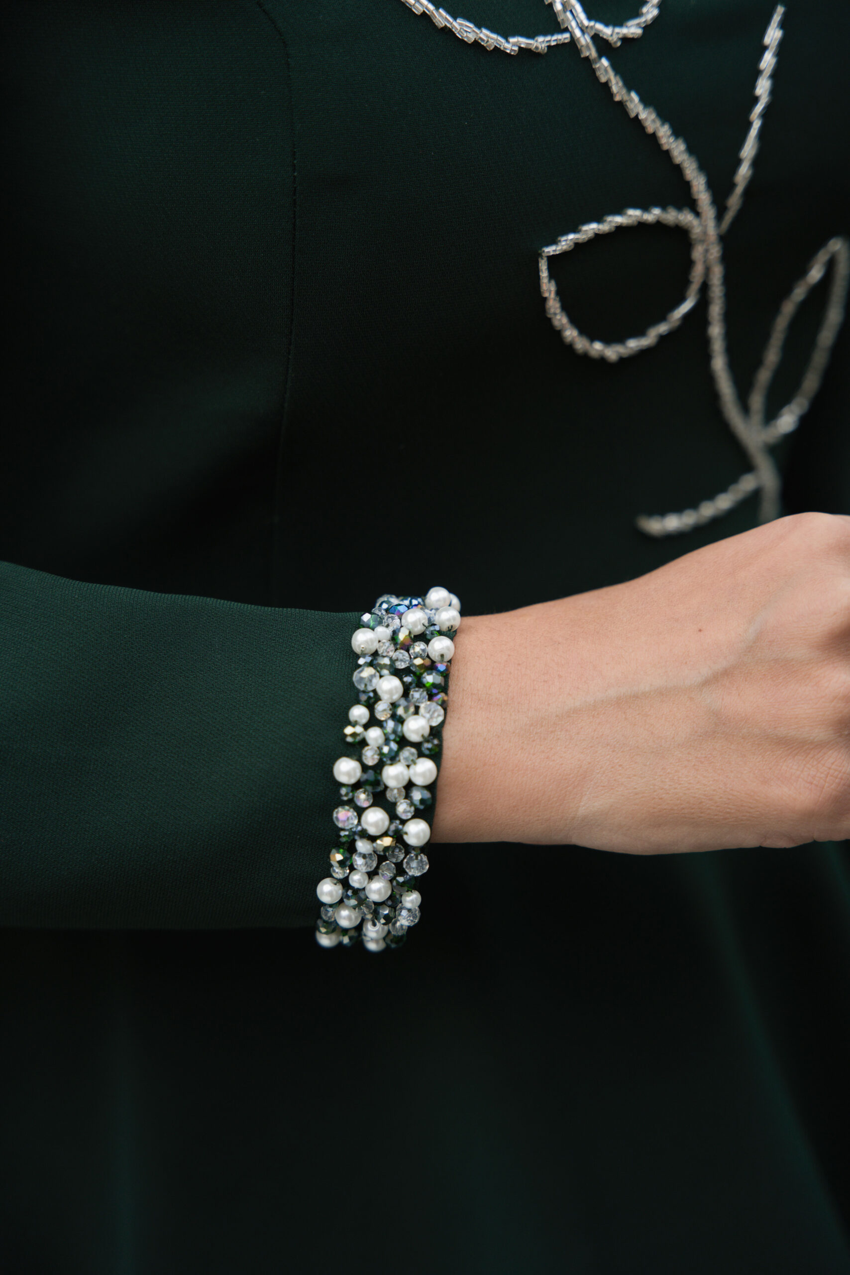Close-up view of dark green couture jacket featuring floral hand-beading and shoulder flower appliqué.
