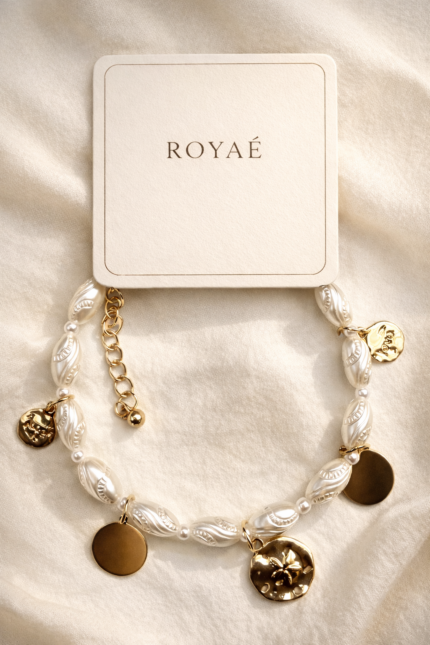 Royaé pearl charm bracelet with gold coin pendants on beige background