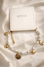 Royaé pearl charm bracelet with gold pendants displayed on satin fabric with branded box